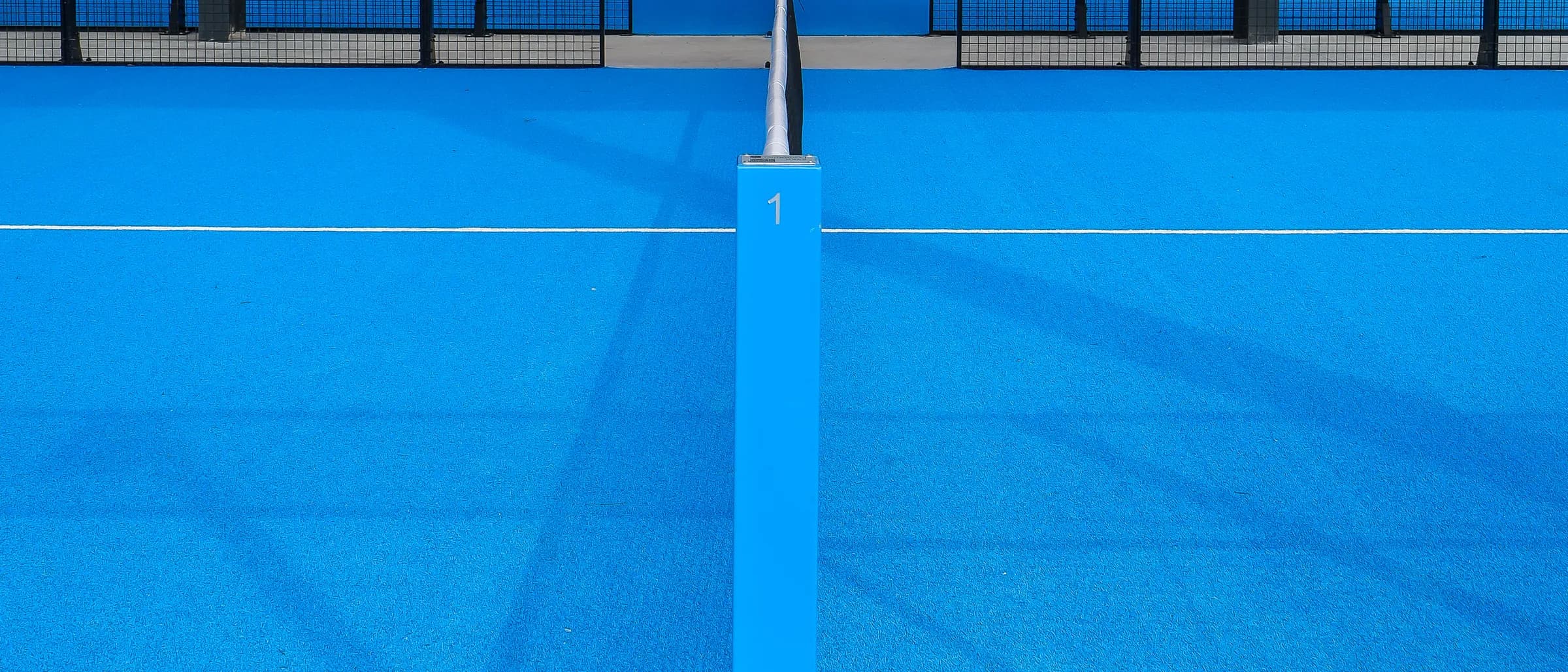 The net post of a blue padel court under a shade canopy