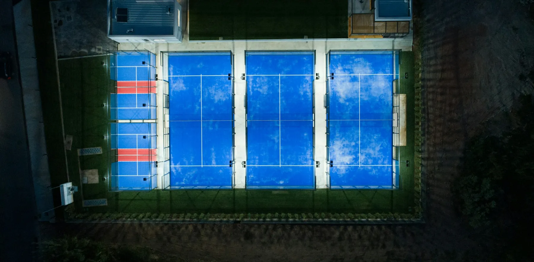 Two padel courts seen from above, glass enclosures catching the light