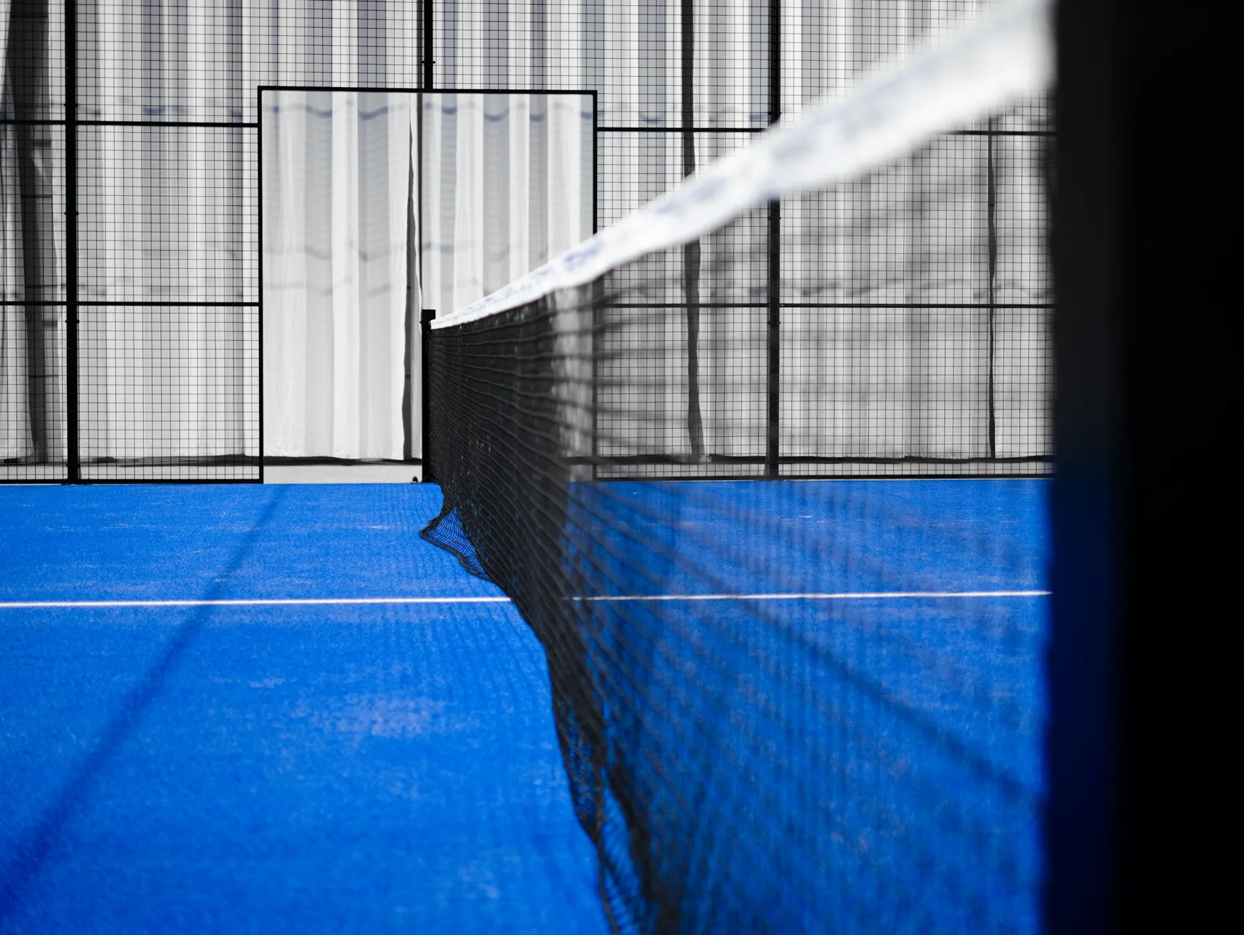 The net meeting the tempered glass wall of a padel court