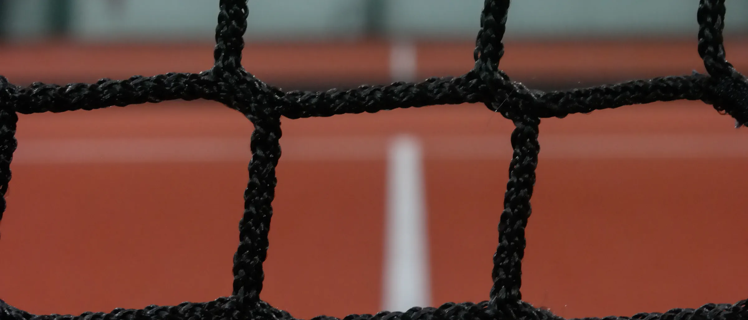 Close view of a padel net over a terracotta surface and its white centre line