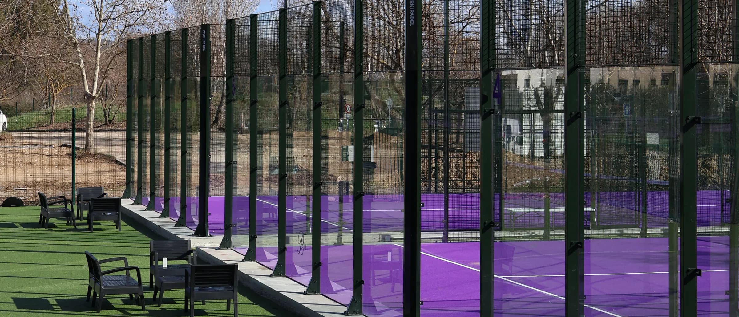 A row of purple padel courts with seating on the turf beside them